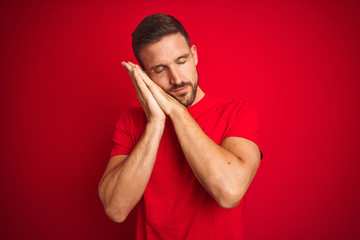 Young handsome man wearing casual t-shirt over red isolated background sleeping tired dreaming and posing with hands together while smiling with closed eyes.