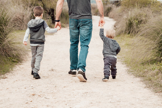 Father and two sons holding hands and walking through nature path