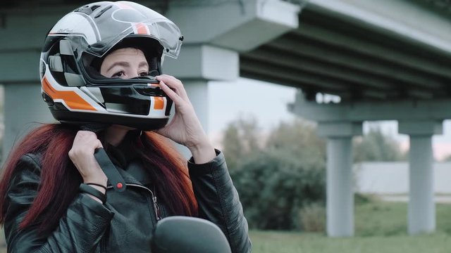 The red-haired girl takes off a motorcycle helmet from the head.