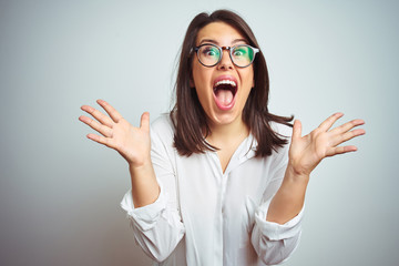 Young beautiful business woman wearing glasses over isolated background celebrating crazy and...