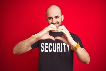 Young safeguard man wearing security uniform over red isolated background smiling in love showing...