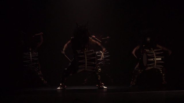 Four artists drummers Taiko in a wig with horns and make-up drum on stage against a dark background. Demons from Japanese mythology.