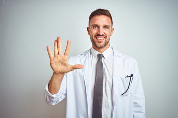 Young handsome doctor man wearing white profressional coat over isolated background showing and pointing up with fingers number five while smiling confident and happy.