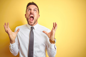 Young handsome business man wearing elegant white shirt over yellow isolated background crazy and...