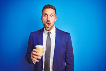 Young handsome business man drinking a coffee on a paper cup over blue isolated background scared in shock with a surprise face, afraid and excited with fear expression