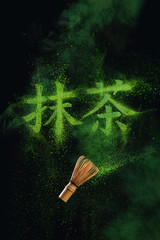 Kanji Matcha written in matcha powder with a bamboo whisk flying in the air. Japanese drink concept on a dark background with copy space