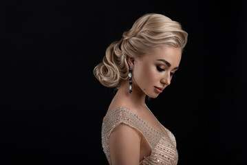 Portrait of a girl on a black background. Wedding hairstyle and makeup. Hanging earrings. Lowered eyes.