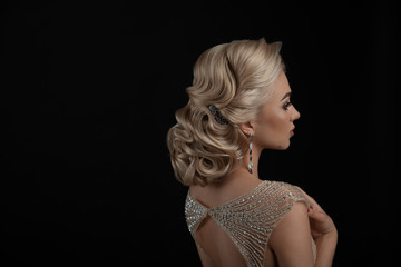Close-up of a wedding hairstyle from the back on a black background. Hanging earrings.