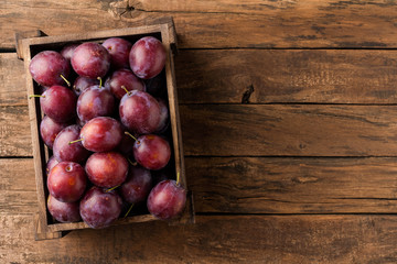 Tasty plums in box on rustic wooden background with copyspace. Top view