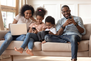 Black family with kids relax on couch using gadgets - Powered by Adobe