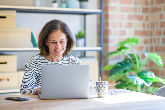Middle age senior woman sitting at the table at home working using computer laptop with a happy face standing and smiling with a confident smile showing teeth