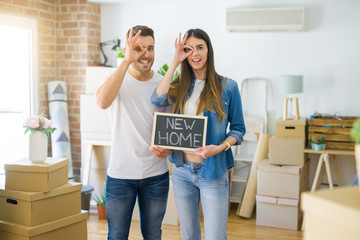 Fototapeta na wymiar Young beautiful couple holding blackboard with new home text at new house with happy face smiling doing ok sign with hand on eye looking through fingers