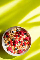 Healthy breakfast with cereal and blueberry and raspberry.Bowl with healthy cornflakes, milk and berries on yellow table.Tasty circle cornflakes.oatmeal with fruits. Diet concept. Copy space