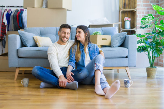 Young beautiful couple sitting on the floor of new apartment, smiling in love happy for moving to a new home