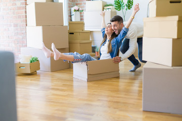 Young couple moving to a new home, having fun riding cardboard boxes