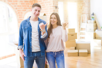 Beautiful young couple moving to a new house smiling with happy face looking and pointing to the side with thumb up.