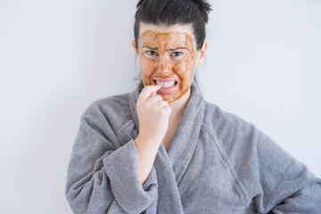 Beautiful young woman wearing cosmetic facial mask as skincare beauty treatment looking stressed and nervous with hands on mouth biting nails. Anxiety problem.
