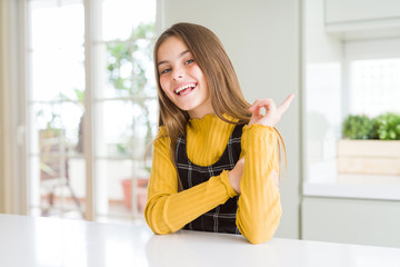 Young beautiful blonde kid girl wearing casual yellow sweater at home with a big smile on face, pointing with hand finger to the side looking at the camera.