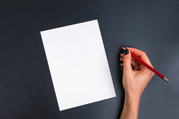 Woman's hand holding red pencil near the blank card on black background