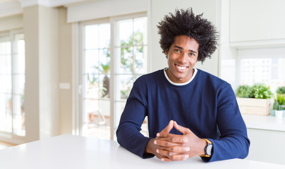 Fototapeta premium Young african american man wearing casual sweater sitting at home with hands together and crossed fingers smiling relaxed and cheerful. Success and optimistic