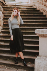 Stylish autumn fashionable image of a girl. Gray blazer, pleats skirt. Blonde woman. Old city background.