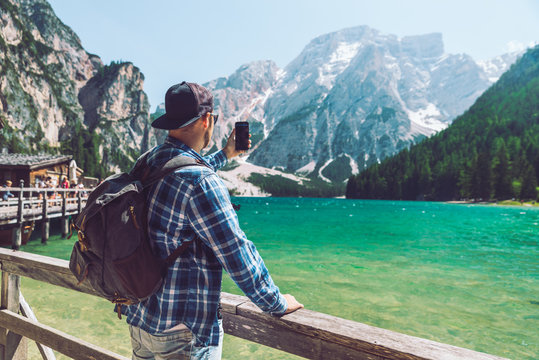 man taking picture on his phone of the lake in mountains