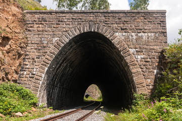 An old railway tunnel trimmed with beautiful historic masonry, among green plants and flowers