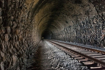 Dark and long railway tunnel with wires and rails extending into the distance