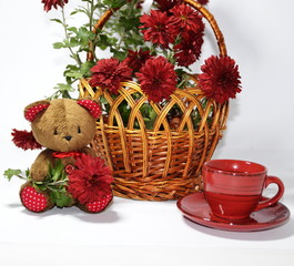 Obraz na płótnie Canvas On the table is a basket of red fresh chrysanthemums, a cup of tea and a cute teddy bear.