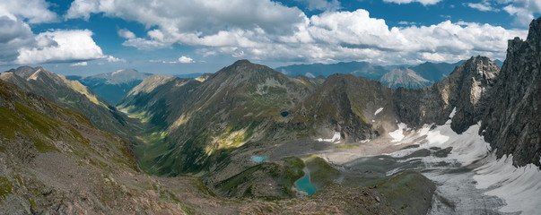 AERIAL; panorama of highland landscape with alpine turquoise lakes, white glacier, dangerous steep rocky slope of mountain ridge Chilipsi; river valley, green high meadows; natural tourism background