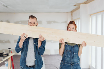 Playful young couple hiding behind a wooden plank