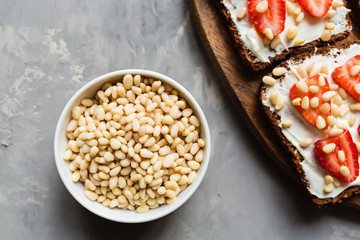 Healthy breakfast. Black bread with strawberry, pine nuts and cheese on gray concrete background. Authentic lifestyle image. Flat Lay, Copy space, top view, overhead, mockup, template. Food concept