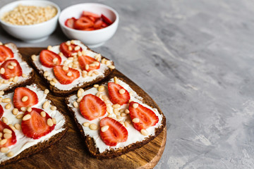 Healthy breakfast. Black bread with strawberry, pine nuts and cheese on gray concrete background. Authentic lifestyle image. Flat Lay, Copy space, top view, overhead, mockup, template. Food concept