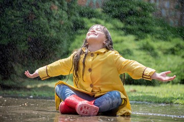 Happy child girl with  rubber boots in puddle