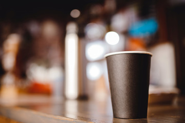 Blurred background paper cup of coffee stands on bar counter in shop, dark light bokeh