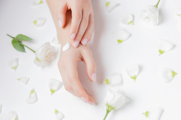 Woman applying hand cream flowers on white background, top view. Concept cosmetic body care, anti-wrinkles, anti-aging spa