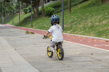 Obraz premium Rear view of a boy wearing a helmet riding a balance bike on a park slate trail