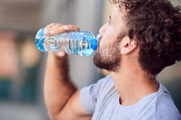 Thirsty sportsman drinking water after exercising / jogging in urban area.