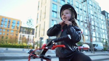 Little girl fixing safety helmet and riding bicycle on street, sport and hobby