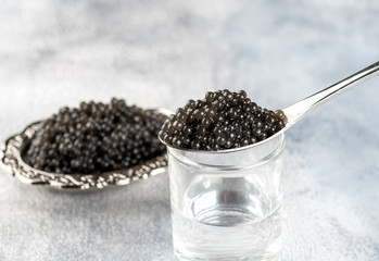 Fototapeta na wymiar Silver spoon of black caviar and glass of vodka on light background