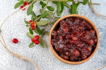 Lingonberry jam or sauce in wood bowl with cranberries, cowberries on light background. Top view.
