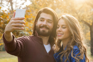 Young couple using cellphone in autumn colored park.