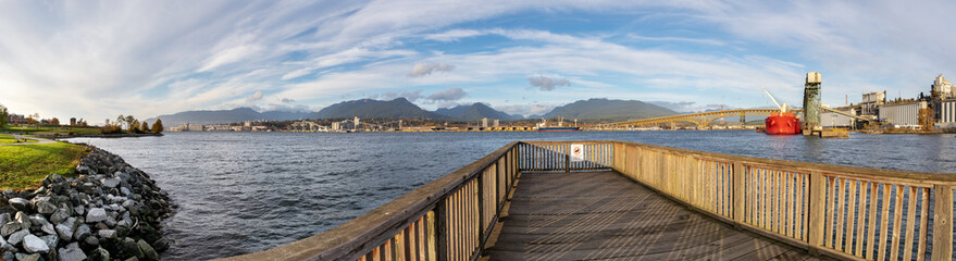 Panorama from New Brighton Park, Vancouver, BC, Canada. Second Narrows Bridge spans over the Burrard Inlet to North Vancouver. Industrial harbor buildings, grain silos, tanker and mountains visible.