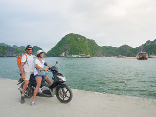 Couple traveling together by motorbike, adult man and woman having fun at Halong Bay and Cat Ba island, famous tourist destination in Vietnam. Scenic sky green mountain peak in the sea.