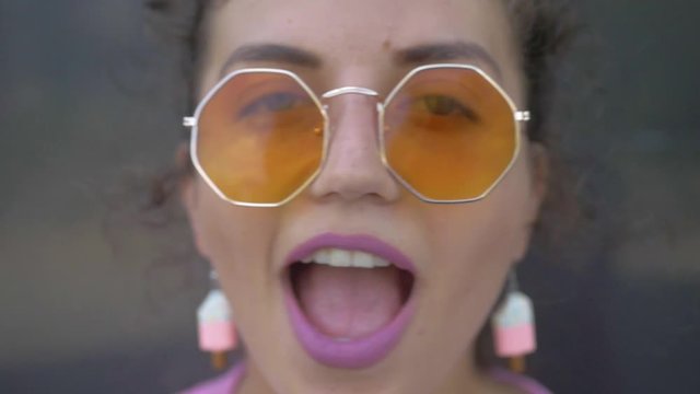 Funny girl sings and looks into the camera. Model with pink lips and yellow glasses looks into the camera. Cheerful young girl will make everyone laugh.