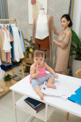 Fashion designer measuring size for tailor made while her baby sitting on table