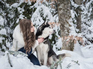 Naklejka na ściany i meble Beautiful girl plays with a dog in a snowy forest.
