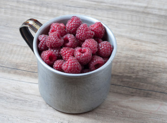 Ripe sweet raspberries in old rustic metal cup.