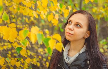 Naklejka premium Portrait of a beautiful smiling woman is standing in the autumn forest between the branches of trees with yellow foliage.