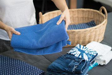 Woman's hands doing the daily chores - laundry. She folded clean clothes, towels and put it in the weaving bamboo laundry basket. Laundry, Softener, House work, Chores, Mommy daily routine concept.